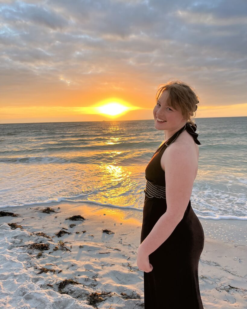 Maggie turned away from camera looking back and smiling while the sun is setting in the background.